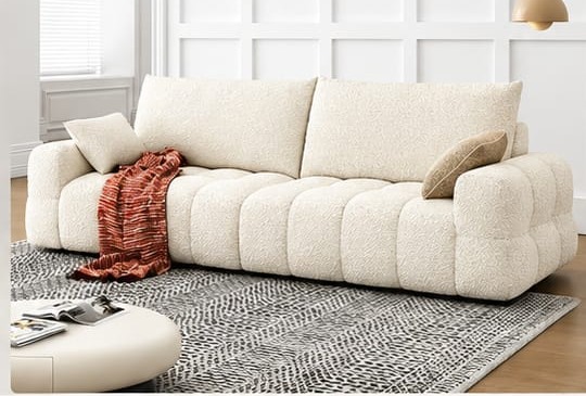 A cream channel-tufted bouclé sofa with a throw across one arm